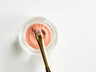 brown makeup brush in front pink powder on glass case