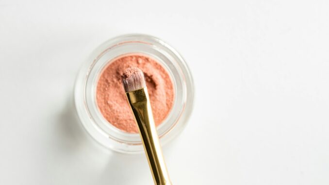 brown makeup brush in front pink powder on glass case